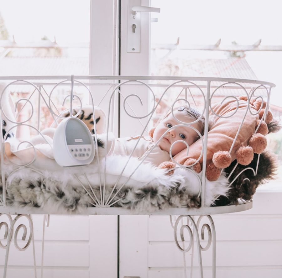 Baby ligt in een wit wiegje bij het raam, met de Numsy Calm aan het voeteneind