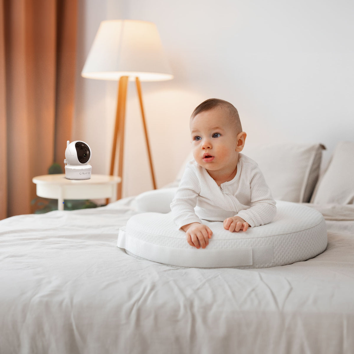 Baby van een paar maanden ligt op bed, met een Numsy babyfoon op het nachtkastje