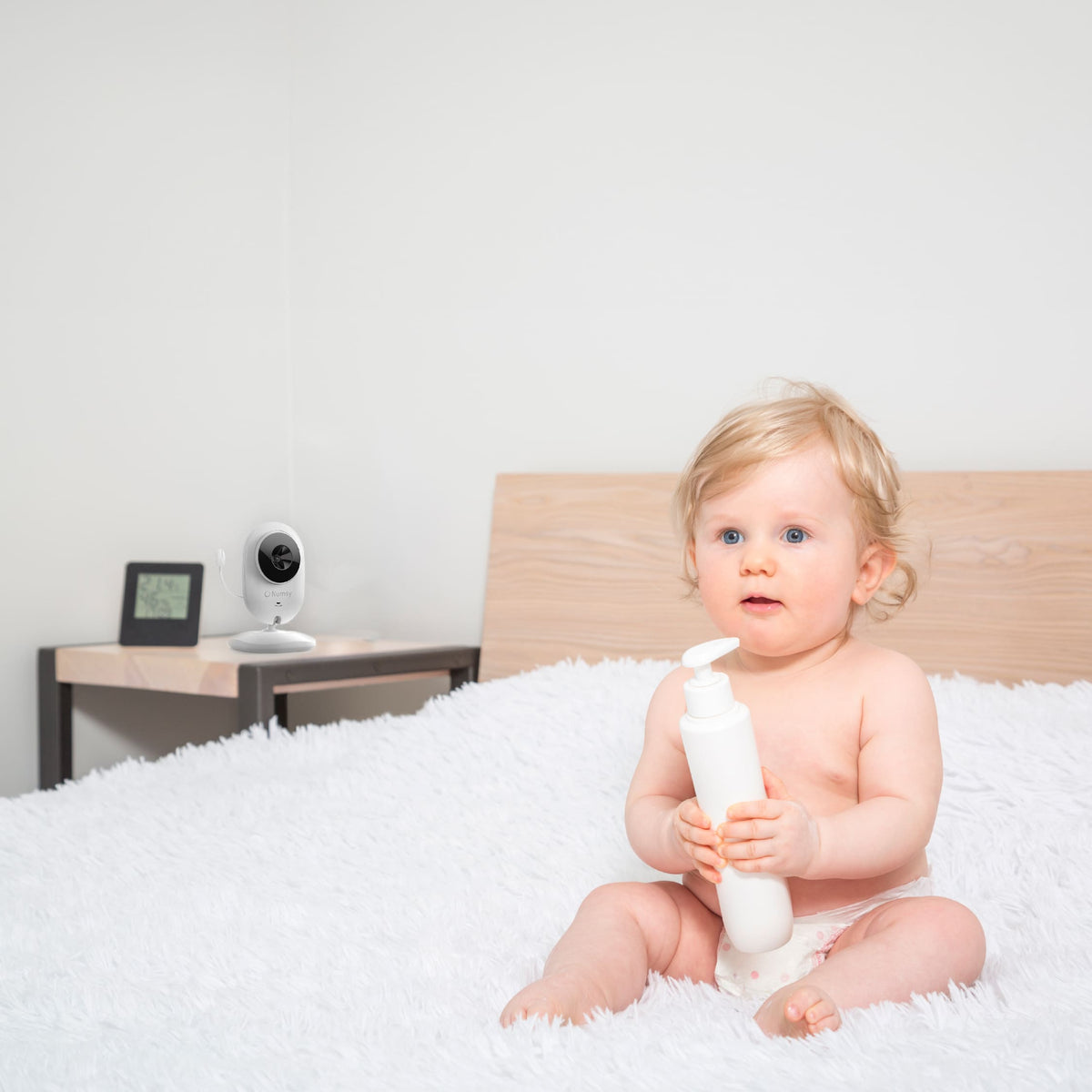 Zittende baby op een zachte deken met een Numsy white noise machine in de handen