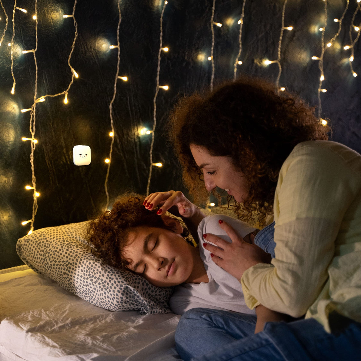 Moeder legt haar slapende kindje in bed bij het warme licht van een Numsy nachtlampje